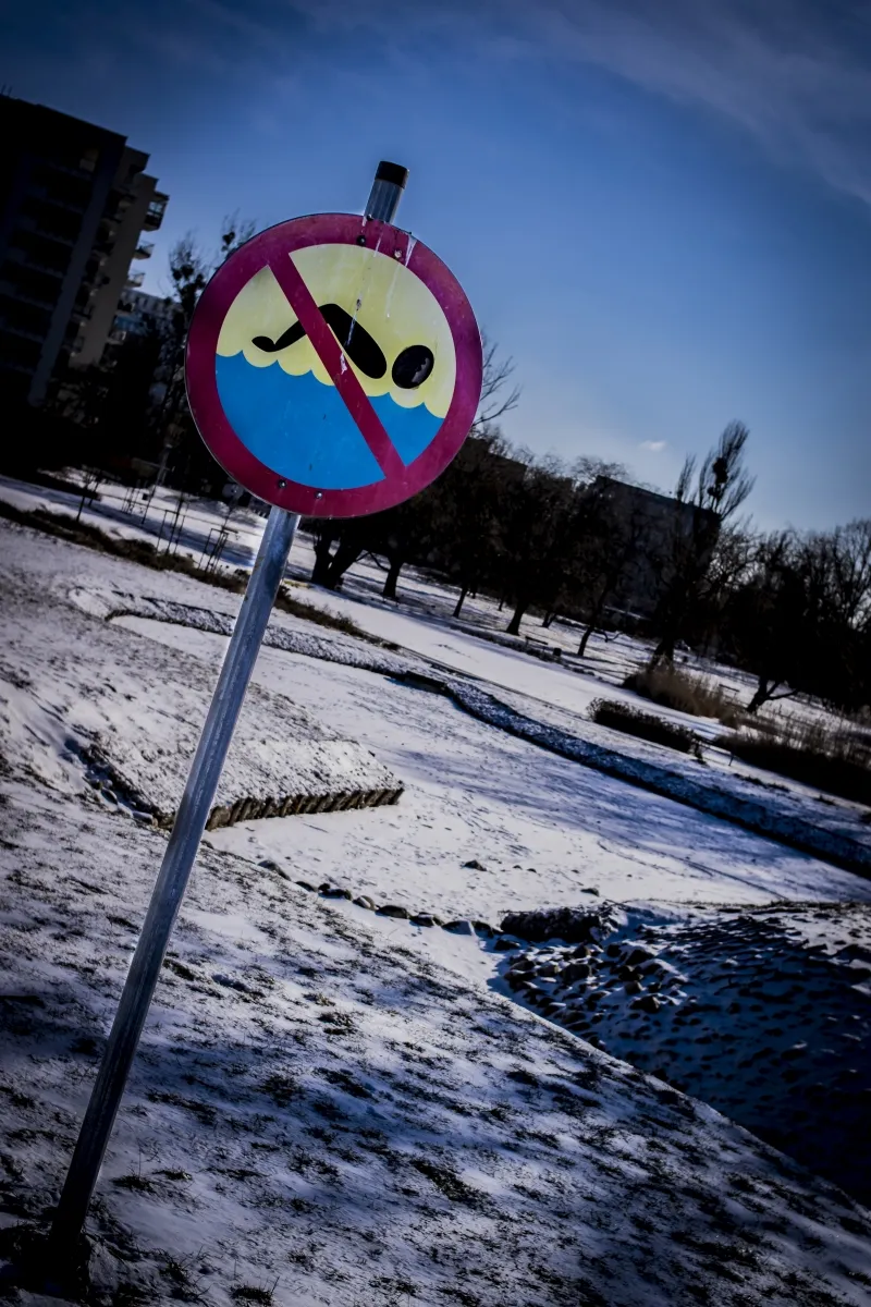 No swimming sign beside a partially frozen snowy pond
